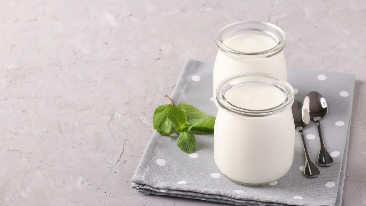 Two jars of yogurt on a gray napkin with spoons.