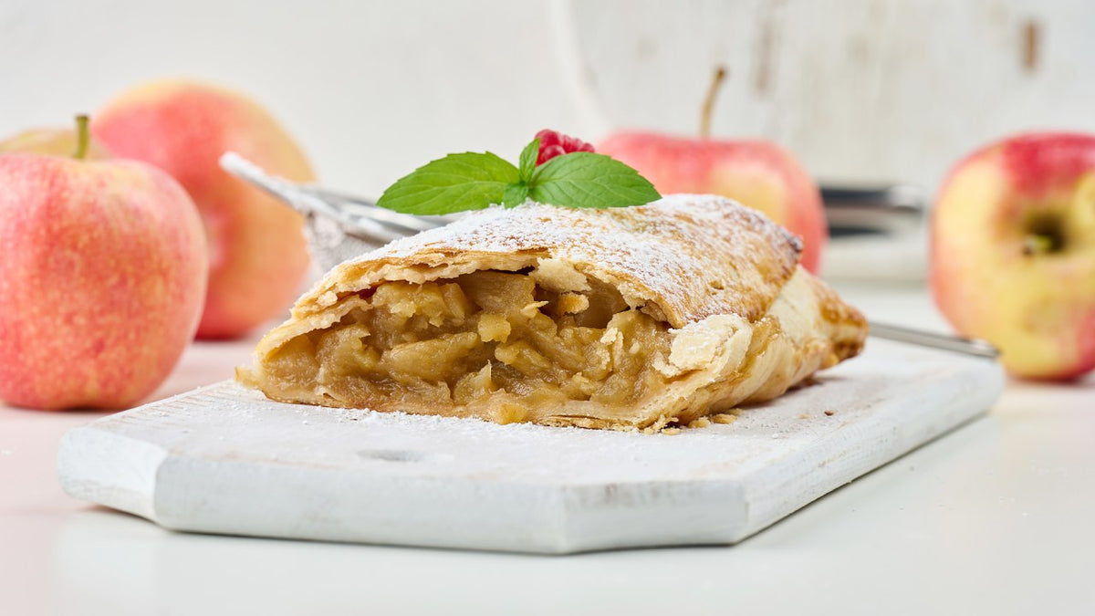 Apple strudel on a white plate with fresh apples in the background.