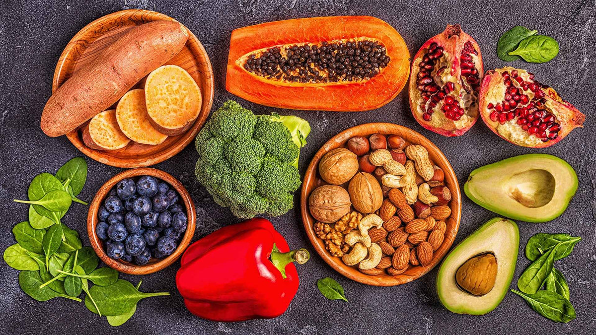 A variety of colorful fruits, vegetables, and nuts arranged on a dark surface.