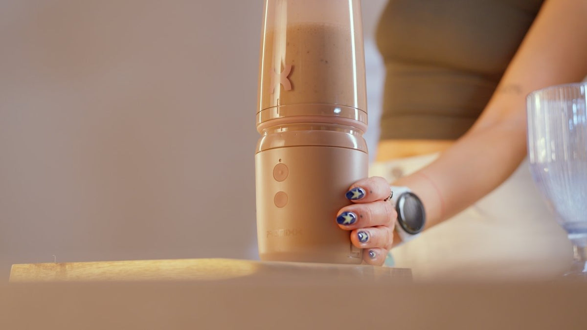 Person holding a blender with a smoothie inside, kitchen setting.
