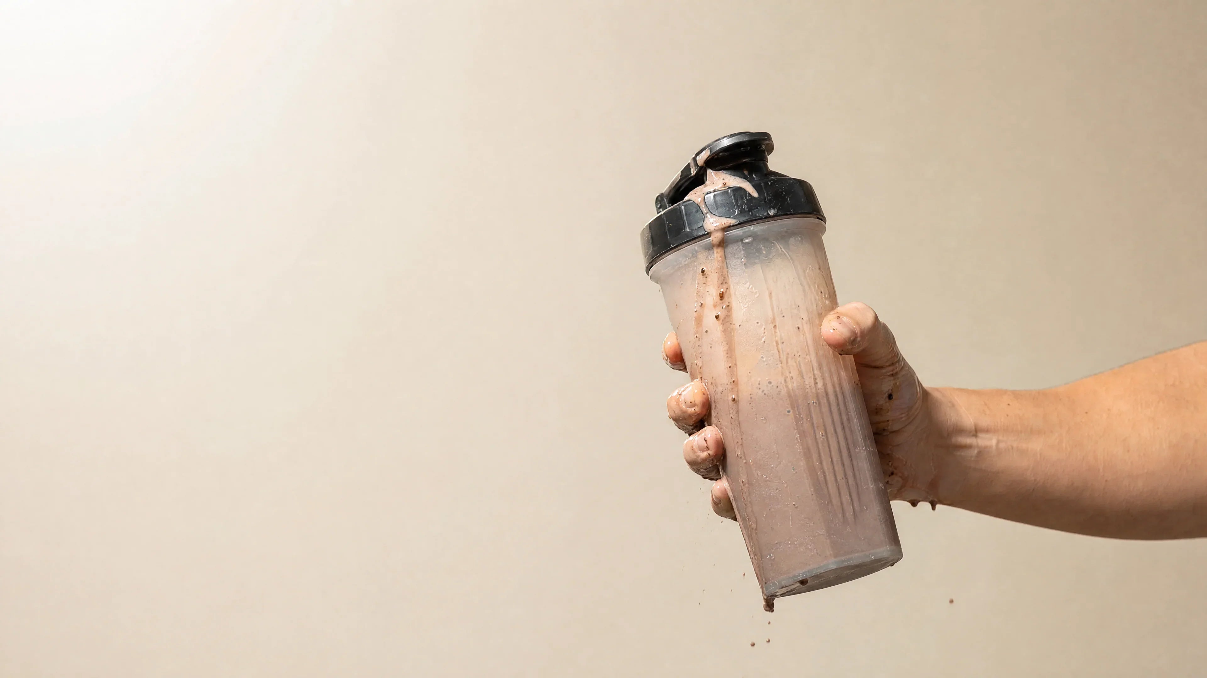 Hand gripping a generic shaker bottle with protein shake spilling over the lid